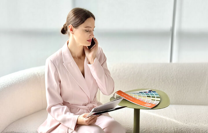 An architect in a light-coloured suit talks on the phone while sitting on a sofa with a catalogue and colour swatches
