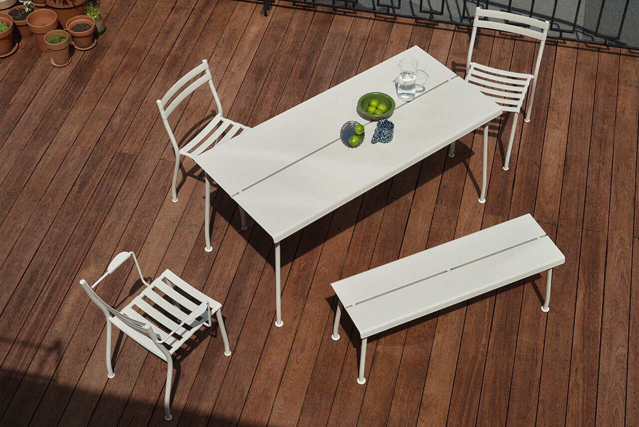 White metal garden furniture set on a wooden terrace – rectangular table, bench and four chairs.
