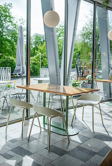 A café space with a wooden table and high stools by large windows overlooking the greenery.