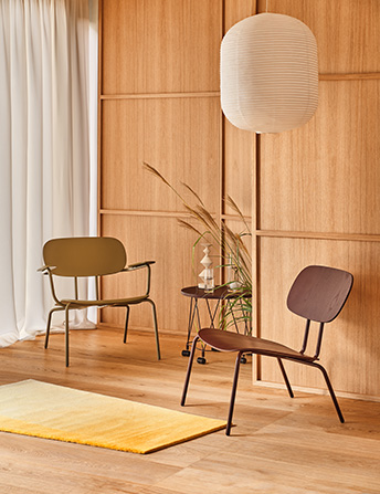 A cosy space with a green and brown chair and a paper lampshade hanging against a wooden wall.