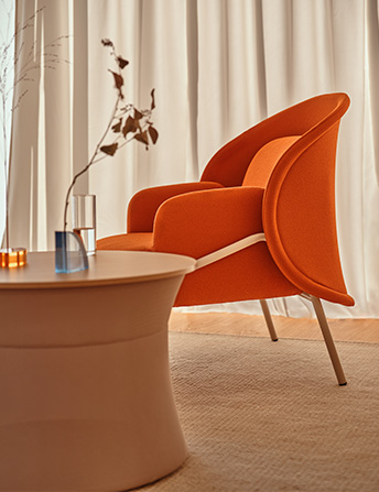 Orange Mesh armchair with rounded back in a smart, bright interior with curtain and low table.