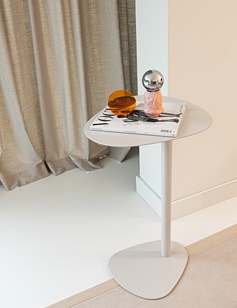 Small white Celo table with decoration in a modern office interior with curtains and carpet.
