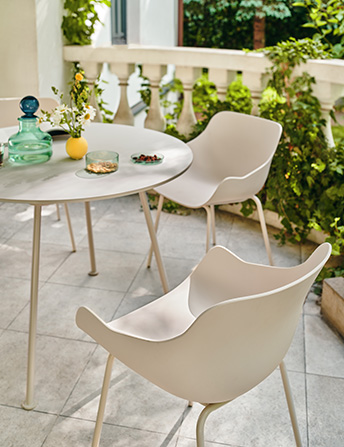 A set of light Baltic chairs at a round table on a terrace surrounded by greenery.