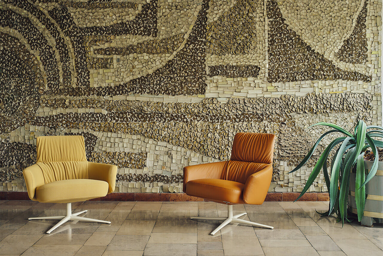 Two modern Toro armchairs, one yellow and one brown, set against a mosaic wall and a potted plant.